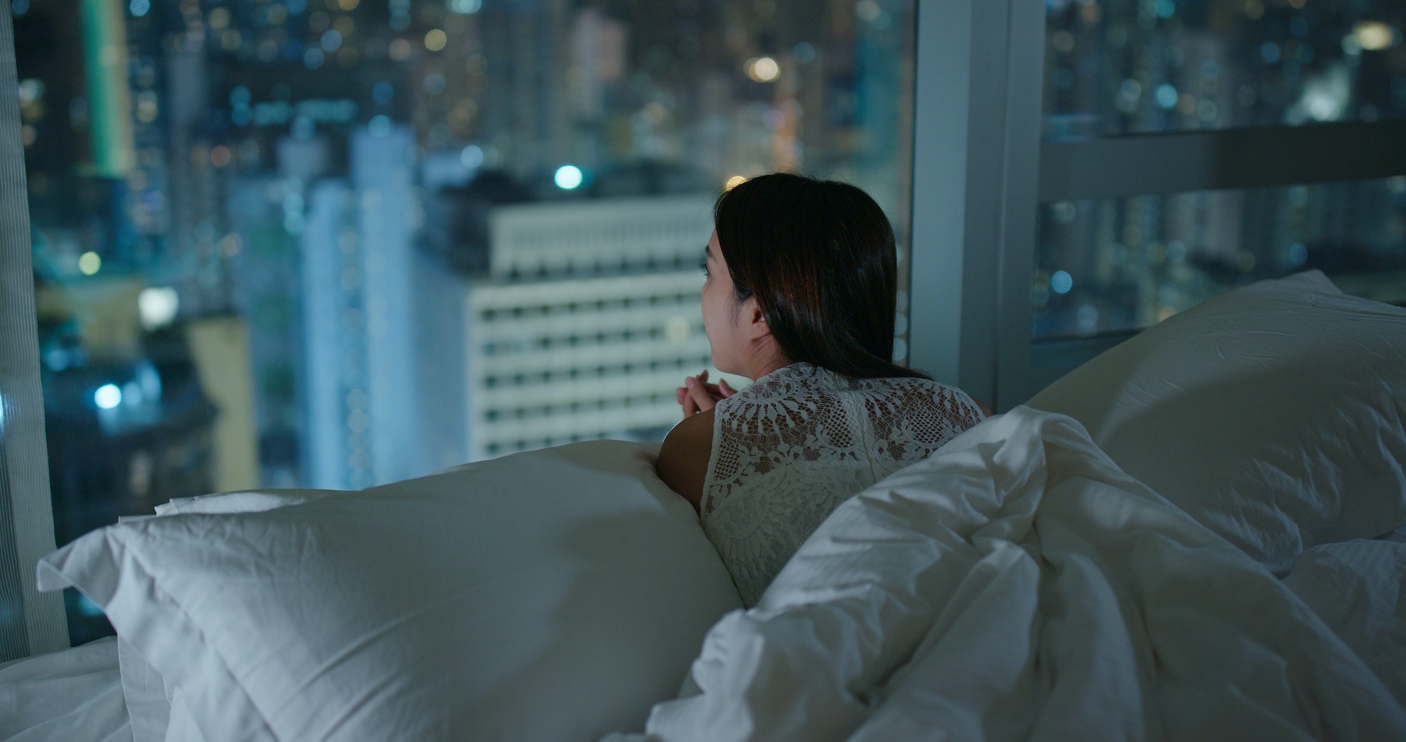 Woman look at the city view and lying on bed at night